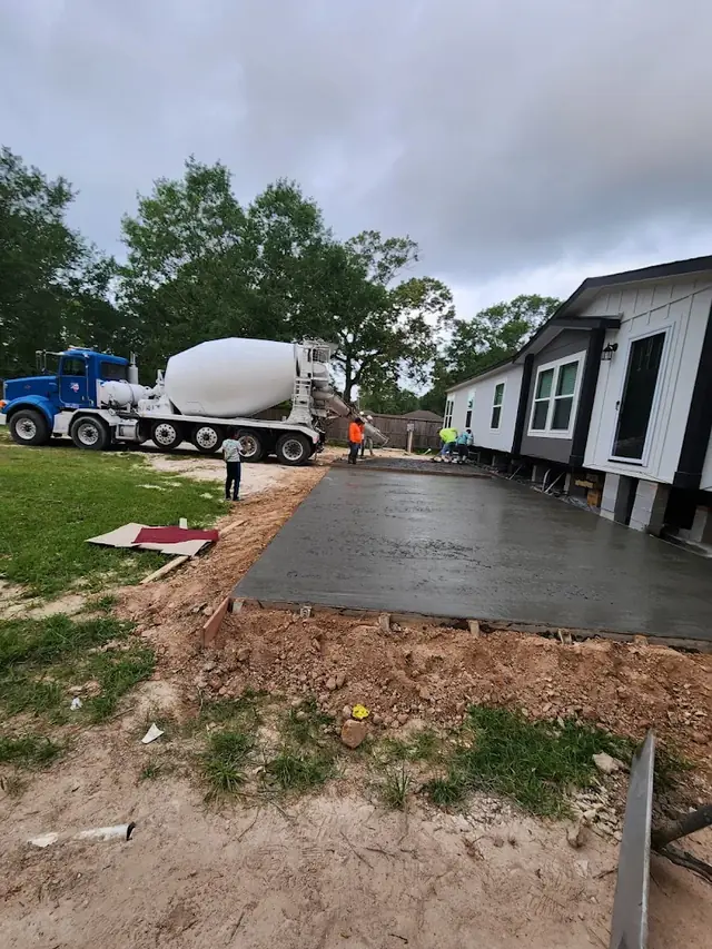 Camión de concreto premezclado vaciando la losa de una entrada junto a una casa